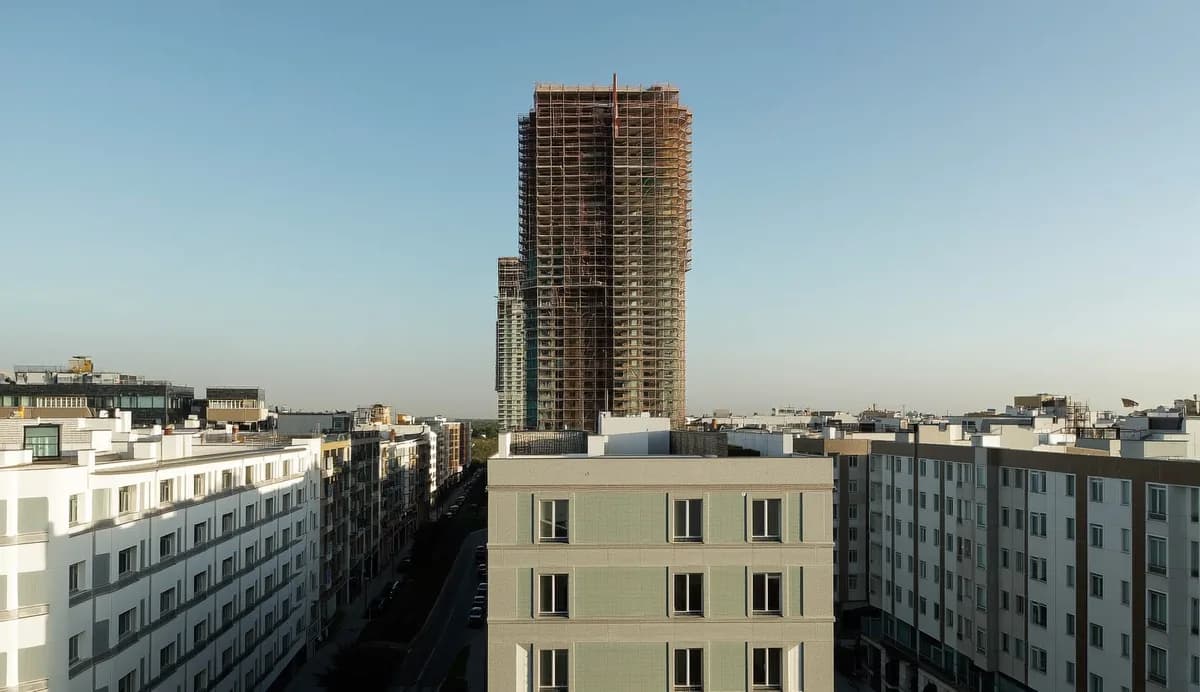 Строящийся жилой комплекс с башенным краном на фоне городской застройки